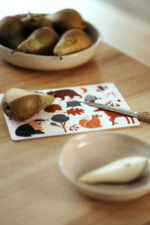 nuukk, Tisch mit Schneidebrett / Frühstücksbrettchen für Kinder, Motiv: Waldtiere. Kind schneidet Birne